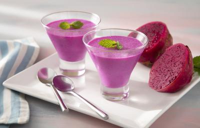 Foto da receita de Mousse de Pitaya e Leite Moça. Observa-se duas taças de vidro com a mousse cor-de-rosa decorada com hortelã em cima de um prato branco quadrado.