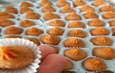 Foto em tons de laranja da receita de brigadeiro de churros servida em várias porções, com destaque para uma unidade sobre os dedos de uma pessoa a frente