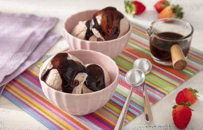 Foto da receita de Sorvete de Morango Caseiro com Calda de Leite Moça e Nescau. Observa-se dois recipientes com duas bolas de sorvete e a calda de chocolate por cima. Morangos decoram a foto.