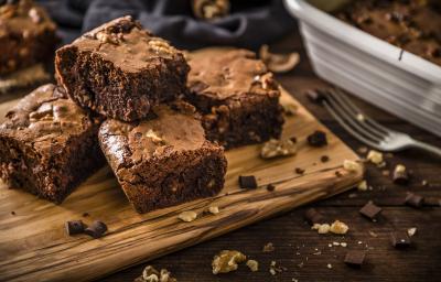 Fotografia de quatro pedaços de brownie feito de farinha de soja, castanha e chocolate. Os pedaços estão sobre uma tábua de madeira perto de um garfo.