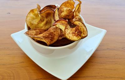 Foto da receita de Chips de Maçã. Observa-se um potinho branco de porcelana com os chips dentro polvilhados de canela.