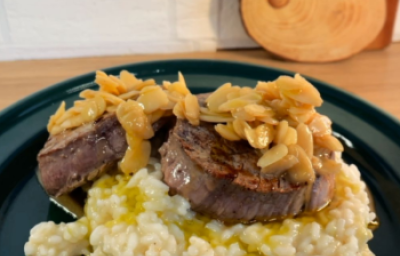 imagem mostra um prato de risoto cremoso em tons beges e por cima 2 medalhões de filé mignon com amendoas laminadas e um molho amanteigado por cima. imagem mostra um prato de risoto cremoso em tons beges e por cima 2 medalhões de filé mignon com amendoas laminadas e um molho amanteigado por cima.
