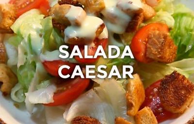 Foto da receita de Salada Caeser. Observa-se um prato com alface americana, tomates cereja, crouton, frango e molho