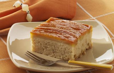 Foto de um prato branco em cima de uma toalha laranja com branco e com um pedaço de bolo de banana dentro com um garfo do lado