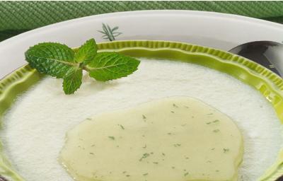 Fotografia em tons de verde em uma mesa com uma toalha verde, um prato branco grande redondo, outro prato branco redondo fundo verde com a mousse de pera com a calda de hortelã.