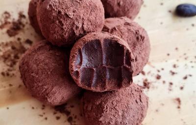 Fotografia de várias trufas de cacau e café passadas no cacau em pó. A trufa da frente foi mordida, e as trufas estão sobre uma tábua de madeira clara.