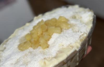 Foto da receita de Delícia de Abacaxi com Doce de Leite. Observa-se a sobremesa em uma travessa oval decorada de coco ralado e abacaxi picado.