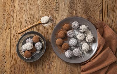 fotografia em tons de marrom e branco de uma bancada marrom vista de cima, contém dois pratos redondos cinza e ambos contém trufas com aveia por cima e chocolate