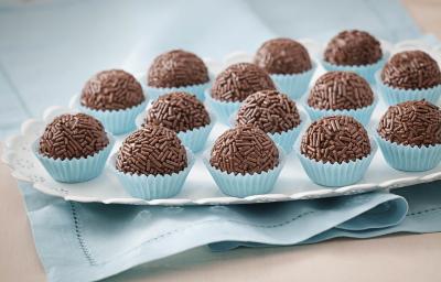 Foto de um prato branco que está em cima de um pano azul com vários brigadeiros dentro de forminhas azuis