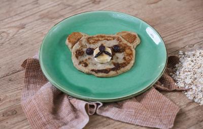 Foto da receita de Panqueca de Banana. Observa-se um pratinho verde e a panquequinha com cara de ursinho.