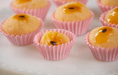 Fotografia em tons de rosa com várias forminhas de brigadeiro ao centro. Dentro de cada forminha existe brigadeiros feitos de maracujá finalizados com geleia de maracujá no topo.