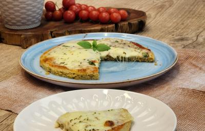 Fotografia em tons de marrom com um prato azul ao centro. Em cima do prato existe uma pizza com massa de Aveia coberta com queijo muçarela e orégano.