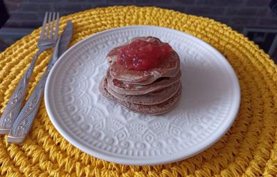 Imagem da receita de Panqueca de batata doce sem glúten com cobertura de geleia de frutas, em um prato branco, sobre uma mesa e ao lado os talheres