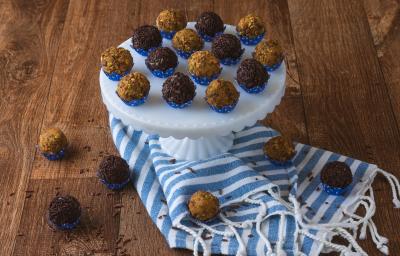 Foto da receita de brigadeiro de pistache da agatha souza, servido em forminhas azuis, sobre um prato em um bancada de madeira com um tecido azul listrado