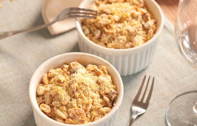 fotografia em tons de cinza, branco e bege de uma bancada cinza vista de cima, contém dois potes redondos e brancos com Crumble de Legumes e queijo ralado por cima, ao lado um garfo para servir.