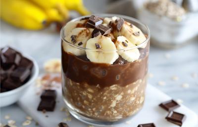 Fotografia em tons de amarelo com um copo de vidro ao centro. Dentro do copo existe uma receita de Overnight Oats com Banana e NINHO Adulto