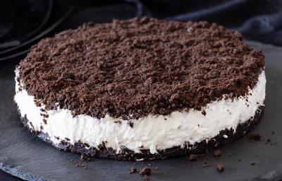 Fotografia de um sanduíche com base e topo de biscoito de chocolate triturado, recheado com creme branco.