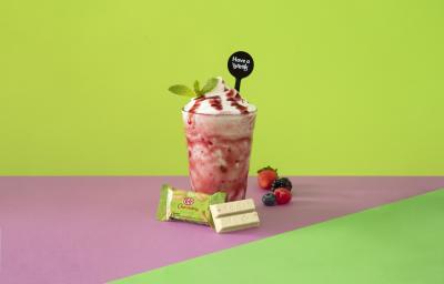 Foto em tons de cor de rosa e verde da receita de smoothie iogurte servida em um copo alto sobre uma mesa cor de rosa com um kit kat hortelã à frente