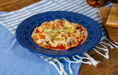 Fotografia em tons de azul com um prato azul ao centro. Em cima do prato existe uma receita de pizza de frigideira feita com frango desfiado, molho de tomate, queijo muçarela e orégano.