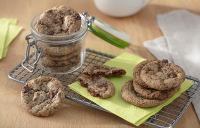 Foto da receita de Cookies Sem Glúten. Observa-se um pote hermético de vidro com os cookies dentro sobre uma grade. Ao lado direito, cookies dispostos sobre um guardanapo verde.