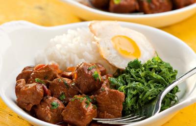 fotografia vista de frente, contém dois recipiente branco e redondo e ambos contém: arroz, couve, pedaços de carne e ovo com um garfo para servir