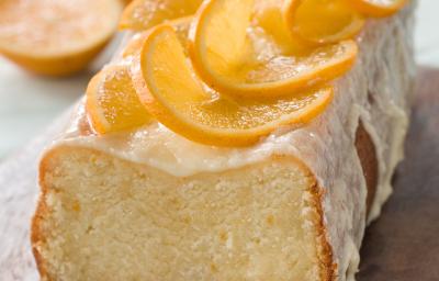 Fotografia de um bolo de laranja feito em forma retangular, com cobertura e rodelas finas de laranja. O bolo está sobre uma tábua de madeira.