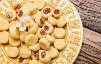 Fotografia de um prato amarelo de vidro sobre uma mesa de madeira. Dentro do prato tem várias unidades de biscoitos amanteigados com goiabada.