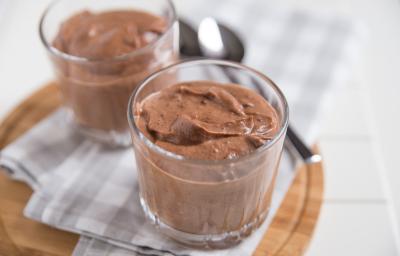 Receita de Mousse de Chocolate da Tia Alzira, tradicional e prático, feito com Chocolate Meio Amargo NESTLÉ CLASSIC, NESTLÉ Creme de Leite e claras em neve, servido em copinhos sobre uma mesa com uma tábua de madeira e colheres ao fundo