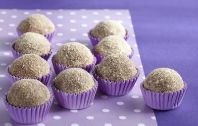 Fotografia em tons de roxo em uma mesa com uma toalha roxa escura, um paninho lilás com bolinhas brancas e vários brigadeiros de cookie dentro de forminhas de docinhos roxa.