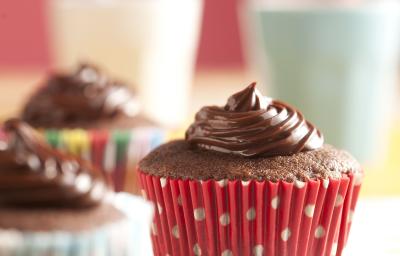 Fotografia em tons de branco e vermelho de uma bancada branca com bolinhas coloridas, sobre ela três cupcakes de Nescau. Ao fundo dois copos com canudos coloridos.