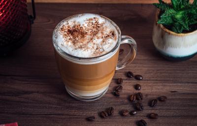 fotografia em tons de marrom e branco de uma bancada marrom vista de cima. Contém uma xicara transparente com café e por cima chantilly com raspas de chocolate.