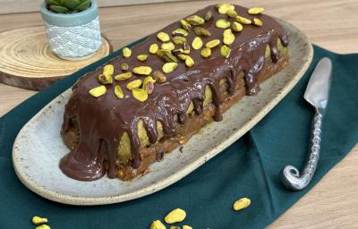 Fotografia de uma sobremesa de cores verde, caramelo e chocolate coberta com chocolate derretido e pistache