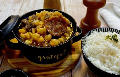 Foto da receita de Grão de Bico com Carnes. Observa-se uma mini panela com grão de bic e linguiça com carne e, ao lado direito, uma mini panela com arroz.