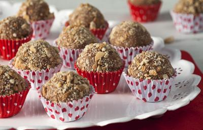 Fotografia em tons de vermelho em uma mesa vermelha com um prato redondo branco com os brigadeiros Classica de palha italiana colocados nele em forminhas de papel brancas e vermelhas com coraçãozinho.