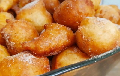 Foto da receita de Bolinho de chuva sem ovo. Observa-se um refratário quadrado de vidro transparente com os bolinhos fritos e polvilhados de açúcar dentro.