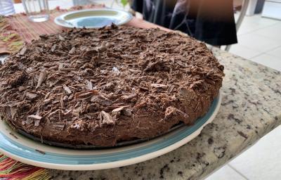 Fotografia de uma torta de chocolate com raspas de chocolate sobre um apoio branco com borda azul.