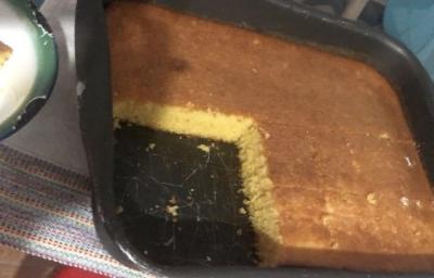 Fotografia de uma forma retangular preta grande com bolo de flocão de milho. Nota-se que faltam quatro pedaços no bolo na forma. Fotografia de uma forma retangular preta grande com bolo de flocão de milho. Nota-se que faltam quatro pedaços no bolo na forma.