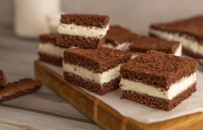 Fotografia de pedaços quadrados de bolo de chocolate recheado com creme de limão, e estão sobre um papel manteiga, apoiado em uma tábua de madeira.