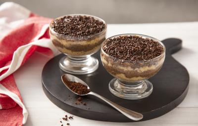 Foto da receita de Bolo de Brigadeiro de Café no Potinho. Observa-se dois potinhos transparentes intercalando uma camada de bolo branco e uma camada de brigadeiro de café. No topo, granulados para decorar.