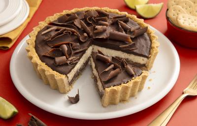 Foto da receita de Torta de Limão com Chocolate. Observa-se uma torta com cobertura de ganache e raspas de chocolate com um pedaço fatiado.