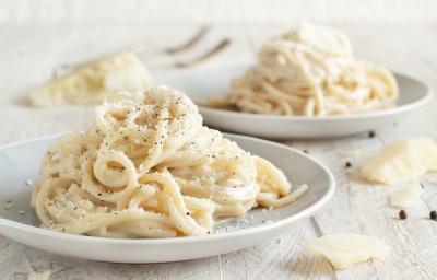 Foto da receita de Macarrão Cacio e Pepe. Observa-se dois pratos com o macarrão espaguete, polvilhado de queijo e pimenta-do-reino preta.