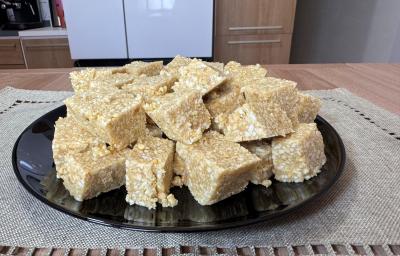 Fotografia em tons claros com vários quadradinhos feitos com amendoim, leite moça e tostines maisena ao centro. Os quadradinhos possuem cores caramelizadas e crocantes de amendoim e tostines Fotografia em tons claros com vários quadradinhos feitos com amendoim, leite moça e tostines maisena ao centro. Os quadradinhos possuem cores caramelizadas e crocantes de amendoim e tostines
