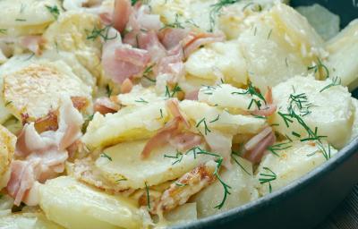 Fotografia de um recipiente com batatas gratinadas, presunto e folhas verdes