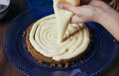 Sobre um prato de vidro de cor azul, há um bolo sendo recheado com um creme de Leite Ninho de cor bege. Para isso, a confeiteira usa um saco de confeitar.