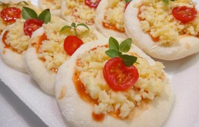 Foto da receita de Mini Pizza. Observa-se os discos pequenos um ao lado do outro, recheados com molho de tomate, queijo, tomate cereja e manjericão.