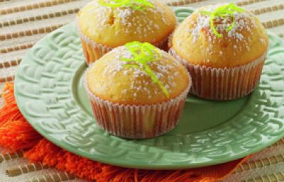 Fotografia em tons de verde, branco e amarelo, ao centro prato verde sobre guardanapo laranja, com três bolinhos decorados com raspas de laranja e açúcar, tudo sobre toalha branca alinhavada.