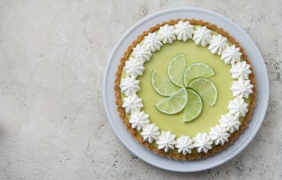 Foto de uma torta limão em cima de um prato branco e com fatias de limão decorando o centro da torta.