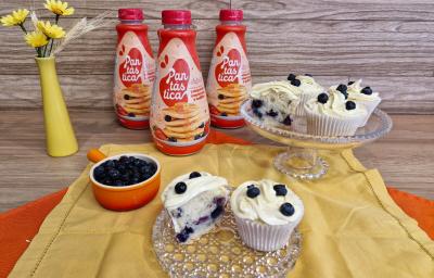 Fotografia em tons de amarelo com dois recipientes de vidro ao centro. Em cima dos recipientes existe vários cupcakes recheados com blueberry e coberto com um creme branco feito de GALAK.