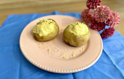 Fotografia em tons de azul e rosa com um prato rosa ao centro. Dentro do prato existe duas batatas recheadas com creme de ASCENDA e polvilhadas com queijo parmesão