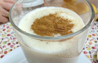 Foto aproximada da receita de Arroz Doce, servido em um taça polvilhado com canela, sobre uma mesa com uma toalha estampada e colorida